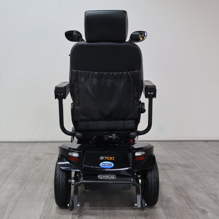 Black Power S700 electric mobility scooter shown from the rear, featuring a padded seat, armrests, and dual rear wheels, photographed in a clean indoor setting with a light gray wall and wood-look floor.