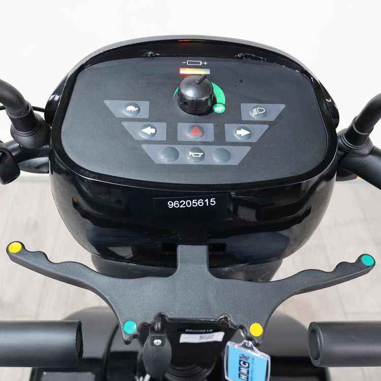 Close-up of a black electric scooter or moped dashboard with a central control panel, handlebar grips, and a small white sticker reading 98205615 on the front.