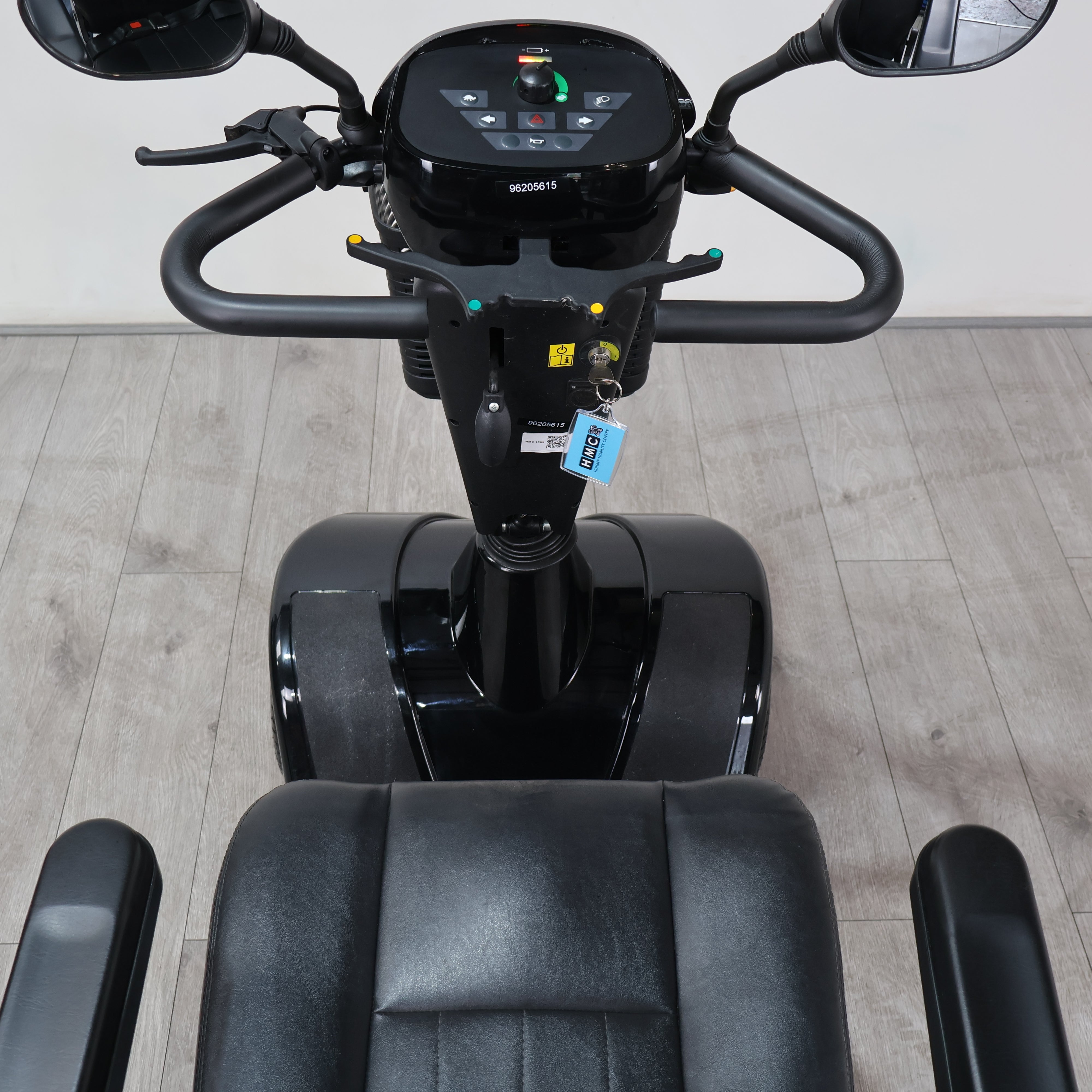 A black Segway-style personal transporter with a digital display screen, handlebars, and a black seat, photographed indoors on a light wood floor against a plain wall.